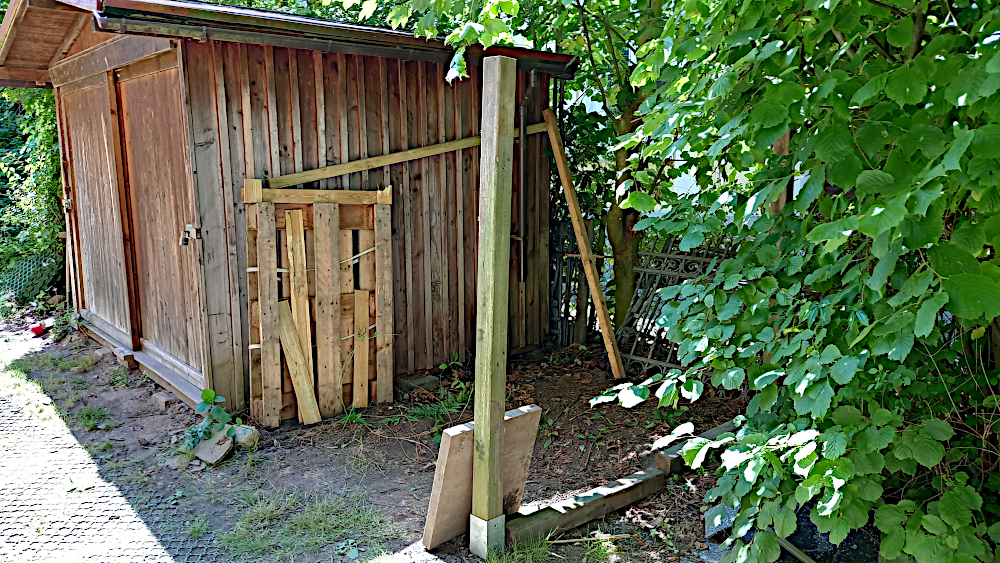 Das Bild zeigt die Nordseite des Gartenschuppens und die Bodenhülsen für die Stützpfähle des Fahrradunterstandes.